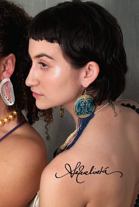 Hand-painted Gemini Mythos statement earrings by Aeterlistá. Large natural mother-of-pearl shell discs featuring symmetrical blue mythological winged figures, finished with long azure blue silk fringe tassels and gold hardware.
